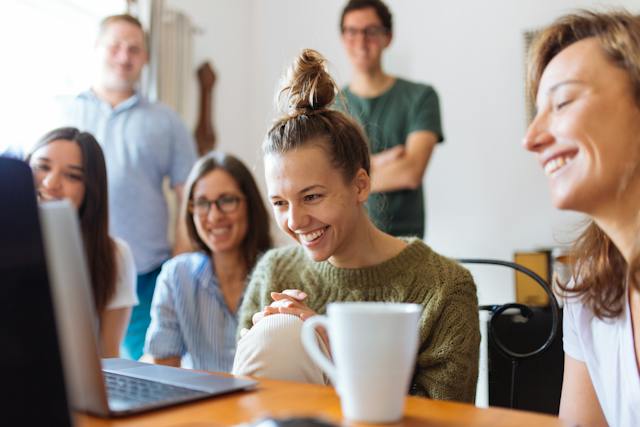 Le persone sono sedute intorno a un computer portatile e ridono guardando i video. 