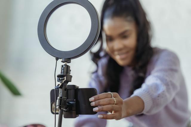 A creator presses a button on her smartphone set up on a tripod. 
