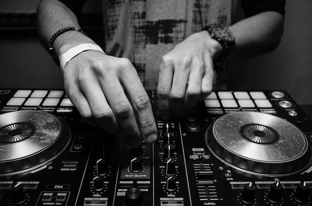 Eine Nahaufnahme der Hände eines DJs, der mit den Bedienelementen eines Audiogeräts spielt. 