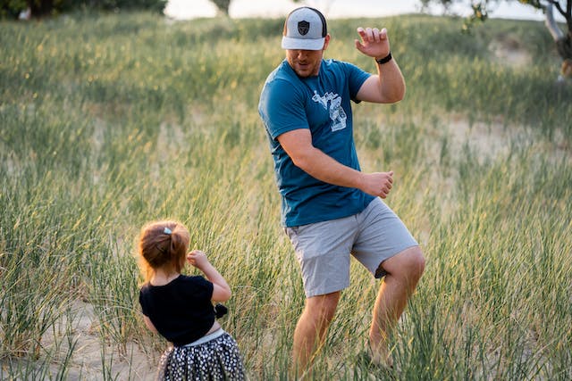 Een afbeelding van een vader en zijn jonge dochter die dansen in een weiland. 