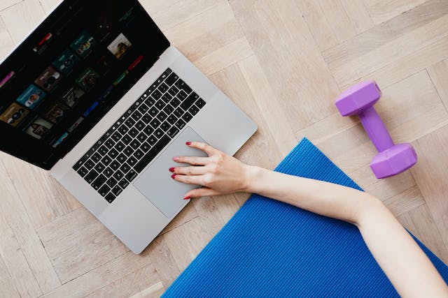 Een vrouw op een yogamat strekt haar arm uit om op haar laptop naar TikTok-oefenvideo's te zoeken. 