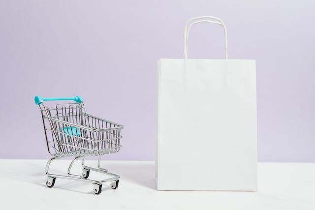 Immagine di un carrello della spesa e di un sacchetto di carta bianco. 