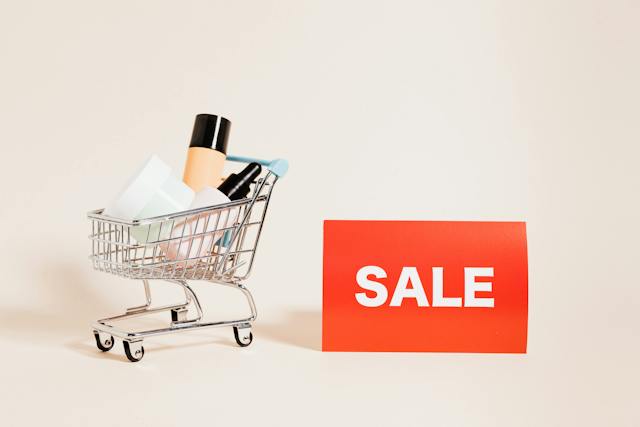 A small shopping cart with beauty products in it and a red and white SALE card beside it. 