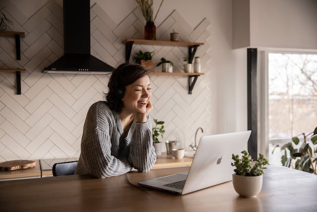 Een vrouw met een koptelefoon op lacht terwijl ze TikTok-video's bekijkt op haar laptop. 