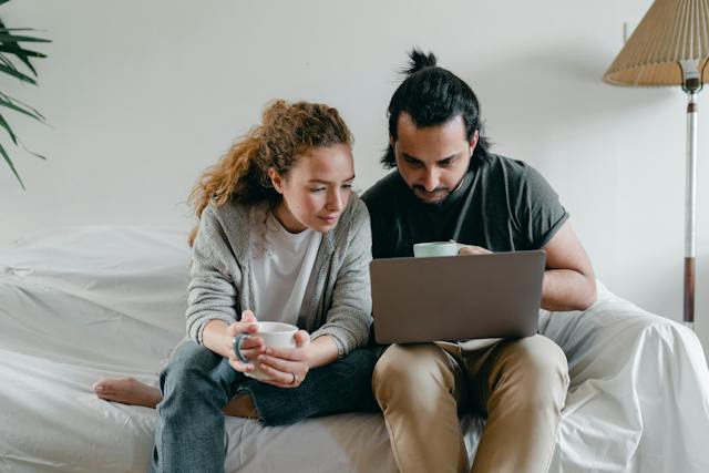 A couple holds their coffee cups and looks at the screen of a laptop.