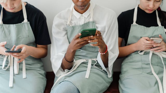 Baristas wearing aprons spend their break time browsing online, using their phones. 