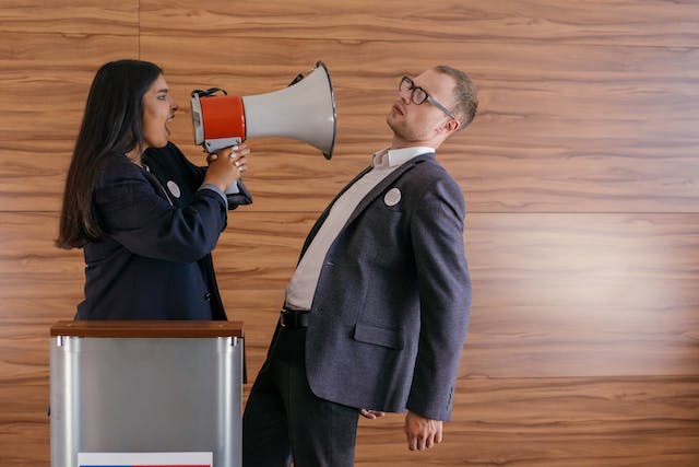A woman uses a megaphone to shout at the man standing in front of her.