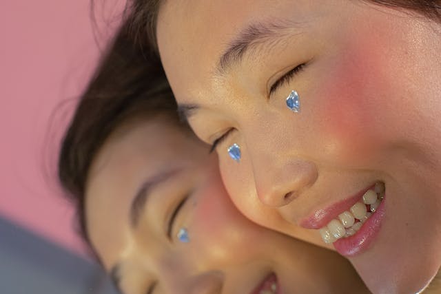 Een close-up en gespiegeld beeld van een lachende vrouw met een stukje diamant onder elk oog. 