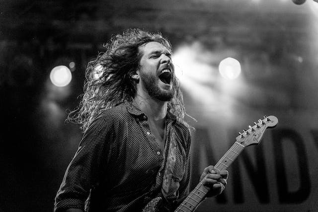 A photo of a man playing a guitar on a stage. 