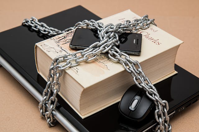 A laptop, book, and smartphone wrapped in a metal chain. 
