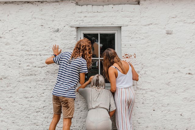 Drie vrouwen gluren door een raam een huis binnen. 