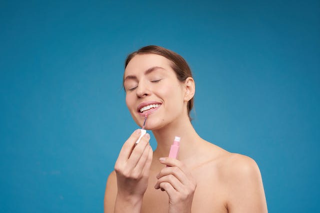 An image of a woman putting on pink lipstick. 