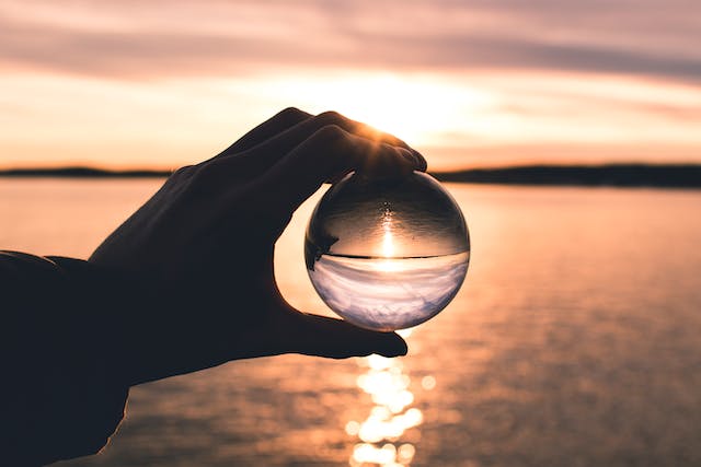 Una persona tiene una sfera di vetro davanti al sole che tramonta per ingrandirlo. 