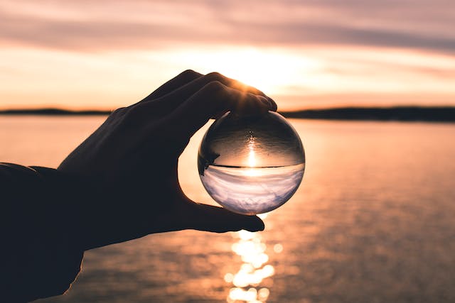 Una persona sostiene una esfera de cristal delante del sol poniente para aumentarlo. 