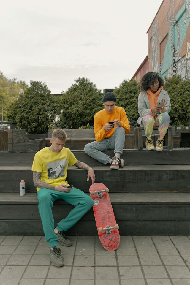 Three skateboarders scroll through their cellphones as they take a break on a set of stairs.
