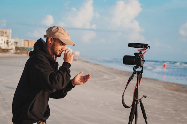한 남성이 삼각대 스탠드를 이용해 해변에서 자신의 모습을 동영상으로 촬영합니다.