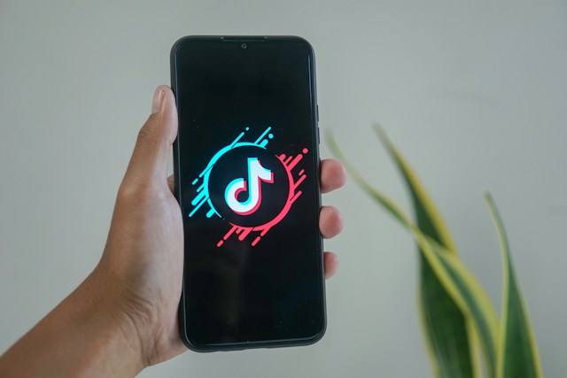 O persoană ține în mână un iPhone care afișează o versiune elegantă a logo-ului TikTok.