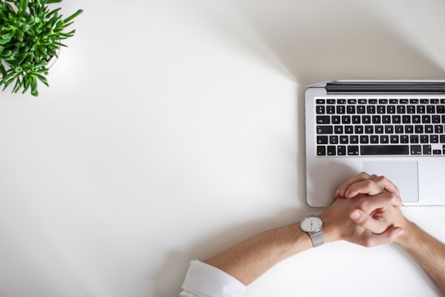 Eine Person, die eine Uhr trägt, sitzt vor einem Laptop.