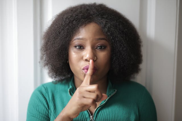 A woman makes the shushing gesture with a finger to her lips. 
