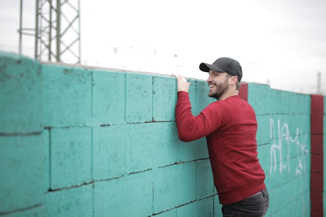 한 남자가 녹색 콘크리트 벽 너머를 바라보고 있습니다.