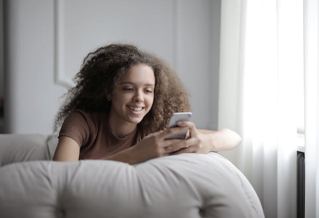 Uma jovem mulher deita-se em um sofá enquanto assiste a vídeos em seu celular. 