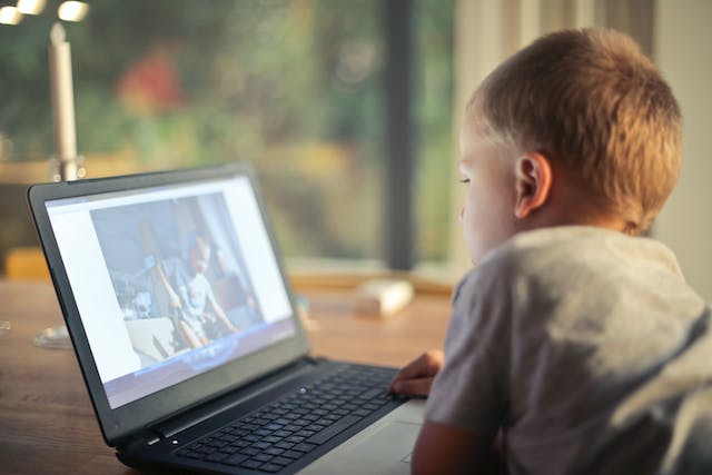 Un băiat se uită la un videoclip pe un laptop.