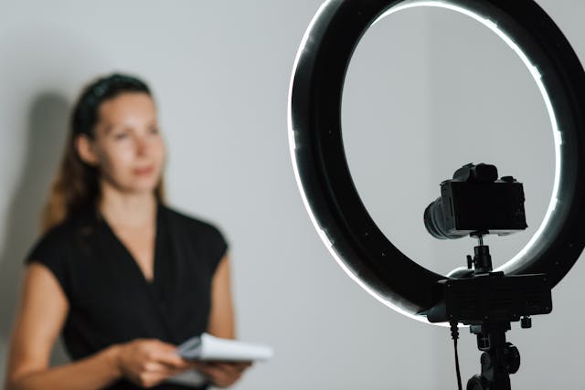 Une femme tient un bloc-notes et se tient devant une lampe torche et un appareil photo numérique. 