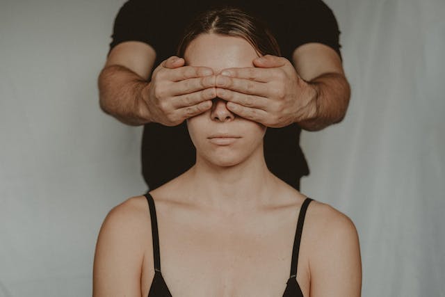 A man covers a woman’s eyes with his hands. 
