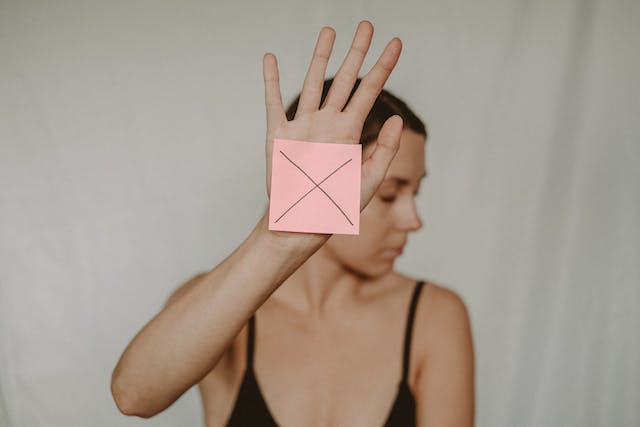 A woman holds up a pink piece of paper with an x on it.