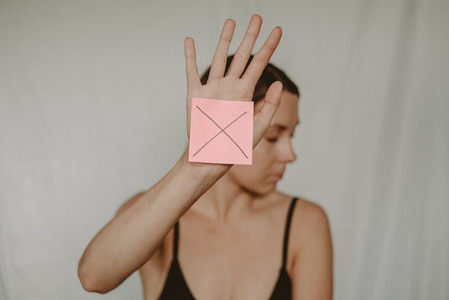 A woman holds up a pink piece of paper with an x on it. 
