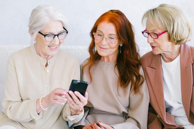 Três mulheres idosas assistem a vídeos em um telefone. 