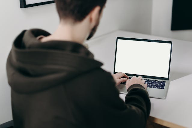 一名男子在笔记本电脑上打字，屏幕显示一片空白。 