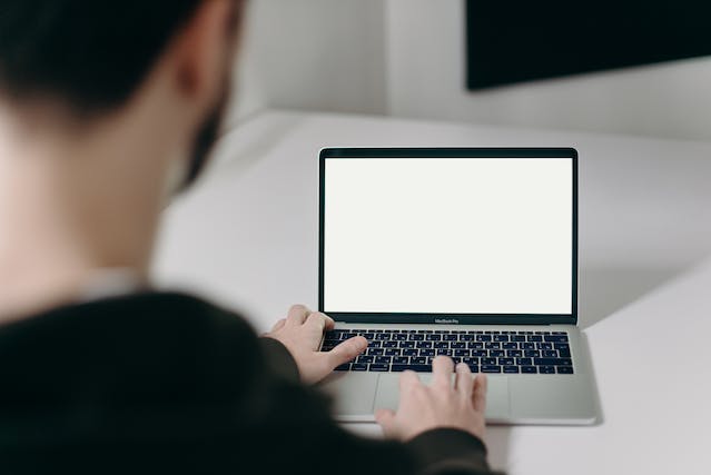 A man scrolls through his laptop, which shows a blank screen. 
