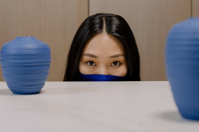 青いフェイスマスクの女性がテーブル越しに覗いている。 
