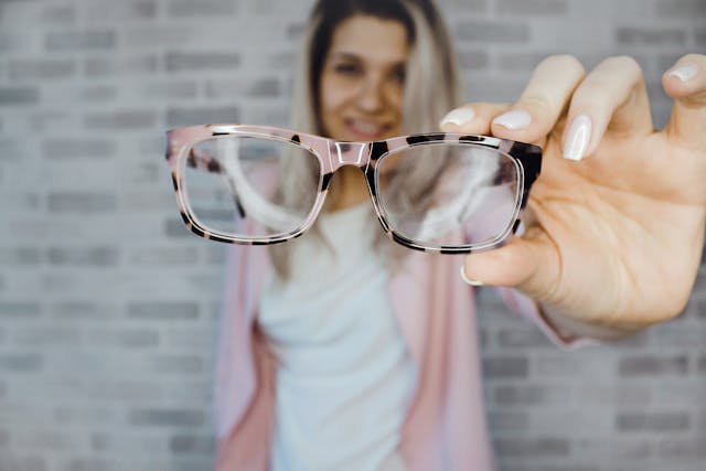 A woman holds a pair of glasses with pink and black frames. 
