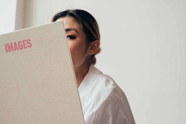 Een vrouw gluurt achter een groot boek vandaan. 