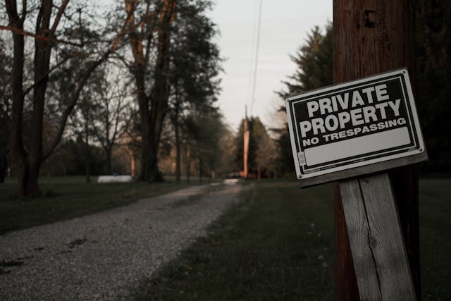 私有地、立ち入り禁止」と書かれた木製の看板が私道の脇に立っている。 