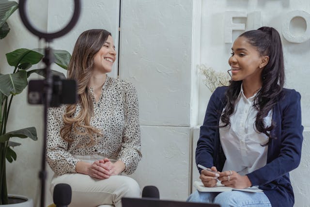 Two women sit down to record an interview.
