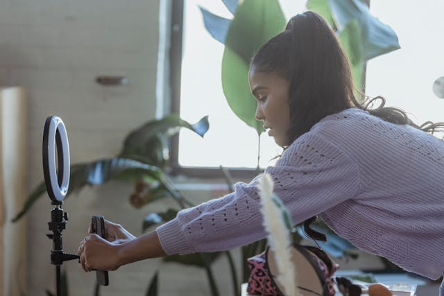 A woman sets up her phone for a LIVE broadcast in front of a ring light. 
