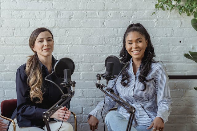 Duas mulheres se sentam em frente a microfones e apresentam um TikTok LIVE. 