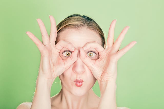 A woman forms the goggle shape with her hands and holds them over her eyes. 
