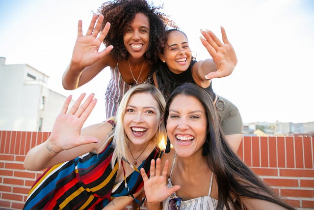 A group of young women waves at the camera. 
