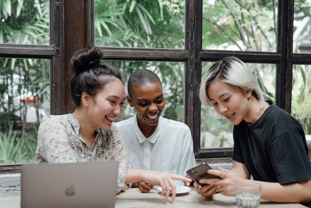 3人の友人がテーブルを囲んでTikTokのビデオを見ている。 