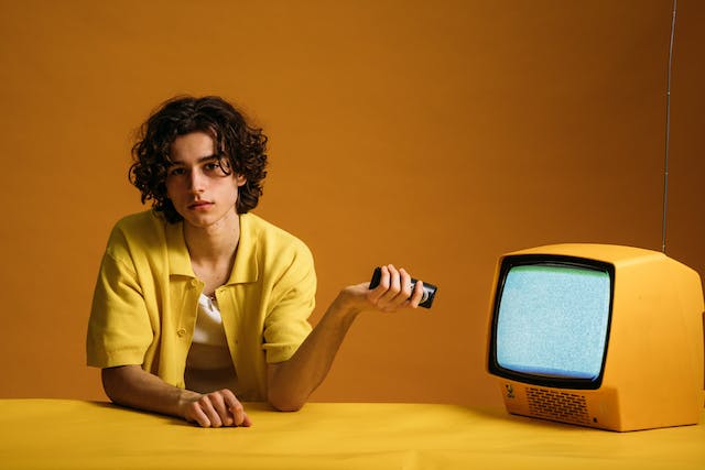 A person points a remote control at a yellow television monitor, which is showing static. 