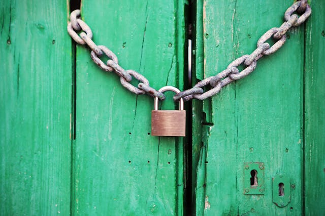 Las puertas de madera verde están cerradas con cadena y candado. 