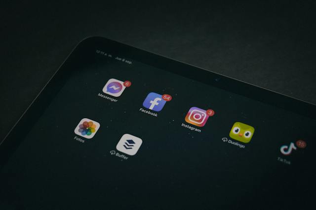 A tablet device shows various social media app icons with notifications. 
