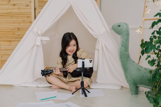 A young creator happily records herself singing and playing the ukulele.
