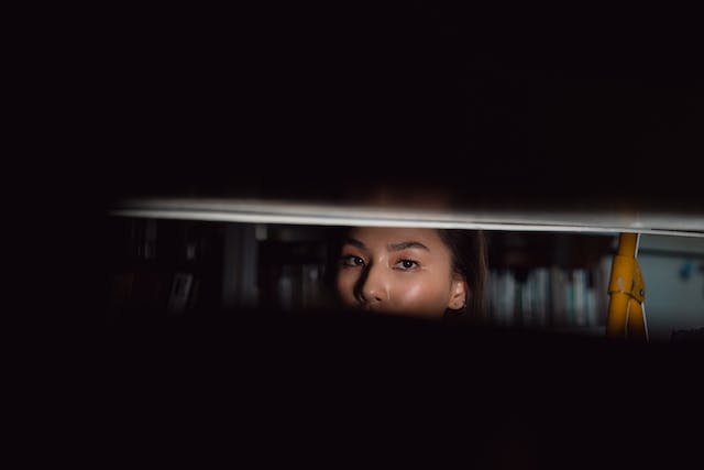 Part of a woman’s face shows through a gap in the window blinds. 