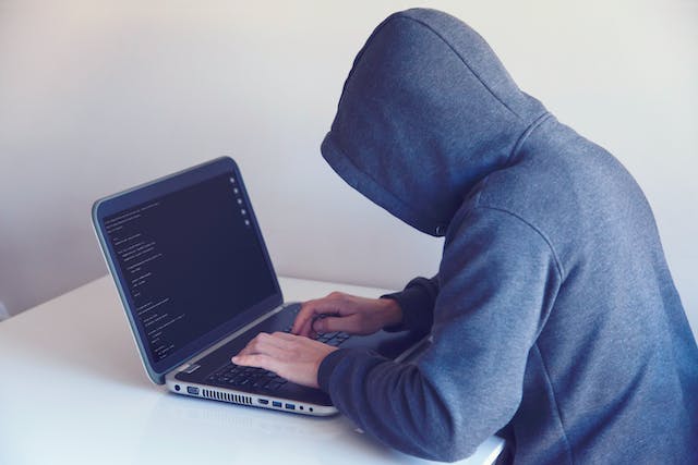 An anonymous person wearing hoodie types on a laptop. 
