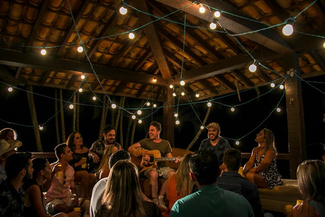 A crowd gathers around a guitarist sitting on a stage. 

